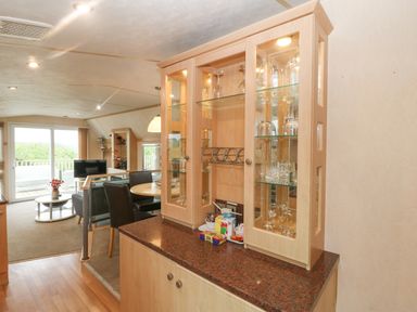 A dining area and living room with glass cabinet and utensils at Coed Llai Lodge in Trearddur Bay