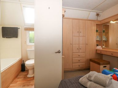 A bathroom with a toilet and bathtub next to a bedroom with a wardrobe and vanity at Coed Llai Lodge in Trearddur Bay