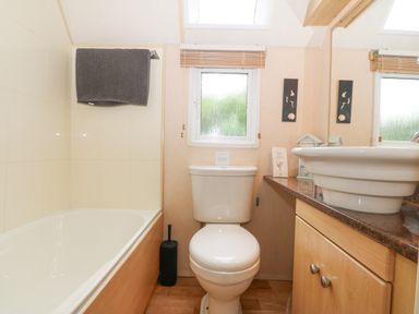 A bathroom with a bathtub towel toilet sink and cabinet at Coed Llai Lodge in Trearddur Bay