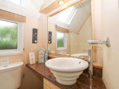 A bathroom with a white sink on a brown countertop and a toilet near a frosted window at Coed Llai Lodge in Trearddur Bay