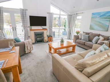 A living room with a fireplace a wall-mounted TV sofas a wooden coffee table and large windows at The Lookout in Stepaside