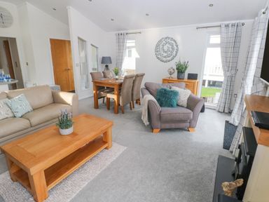 A living room with beige and gray sofas a wooden coffee table a dining table with chairs and windows with curtains at The Lookout in Stepaside