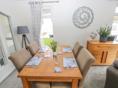 A dining room with a wooden table set for four with placemats and wine glasses and beige chairs at The Lookout in Stepaside