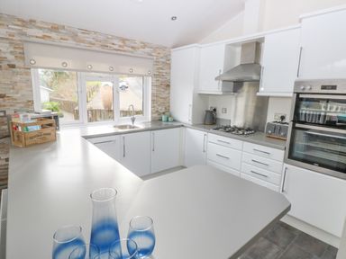 A kitchen with white cabinets a gas stove an oven a toaster and a sink by a window with stone tiled wall at The Lookout in Stepaside