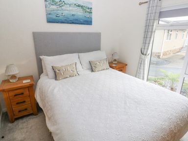 A bedroom with a double bed with white bedding and pillows two wooden bedside tables with lamps and a window with curtains at The Lookout in Stepaside