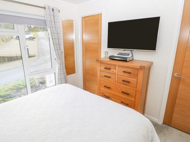 A bedroom with a white bedspread a wooden chest of drawers a wall mounted television and two wooden doors at The Lookout in Stepaside