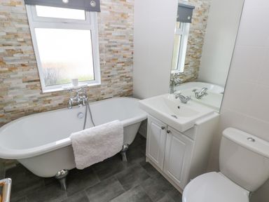 A bathroom with a freestanding bathtub a sink with cabinet a toilet and a frosted window at The Lookout in Stepaside