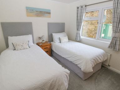 A bedroom with two single beds a wooden nightstand between the beds and a window with checkered curtains at The Lookout in Stepaside