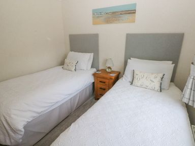 A bedroom with two single beds with grey headboards a wooden nightstand with a lamp and a beach painting on the wall at The Lookout in Stepaside