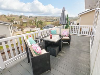 An outdoor balcony with black wicker chairs with cushions and a table with a closed umbrella at The Lookout in Stepaside