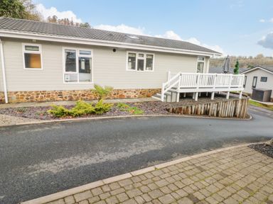 An exterior view of a beige single-story house with a stone foundation a white railing deck a paved driveway and landscaping at The Lookout in Stepaside