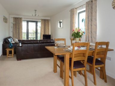 A dining table with four chairs and set tableware next to a living room with dark leather sofas and large windows at Tyack in Charlestown