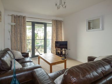 A living room with brown leather sofas a wooden coffee table a television and glass doors leading to a balcony at Tyack Charlestown