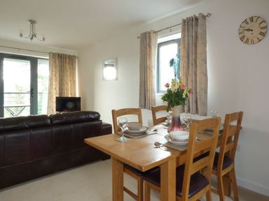 A dining table set with plates glasses and a vase of flowers next to a window with curtains and a dark sofa in a living room at Tyack in Charlestown