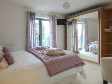 A bedroom with a bed covered with folded towels and purple bedding next to floral curtains and a mirrored wardrobe at Tyack in Charlestown