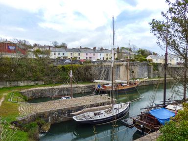 A harbor with historic sailing ships docked near stone walls and houses at Tyack in Charlestown