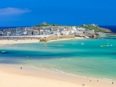 A beach with people walking on sand and turquoise water and a town with houses and a hill in the background at Birch in Truro