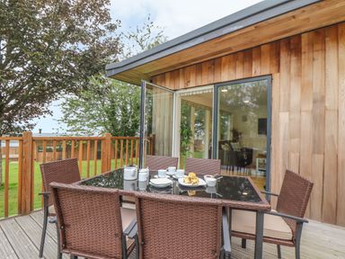 An outdoor dining area with a glass table and wicker chairs on a wooden deck outside a wooden house at Birch in Truro