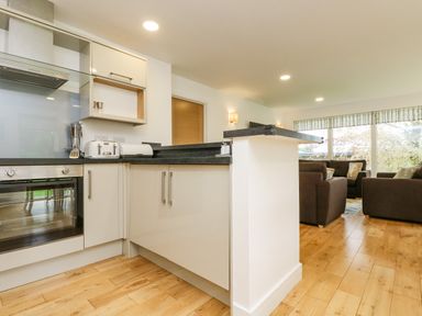 A kitchen with white cabinets and black countertops next to a living room with brown sofas and large windows at Birch in Truro