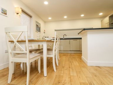A dining area with a wooden table and white chairs next to a kitchen with cabinets and a sink at Birch in Truro