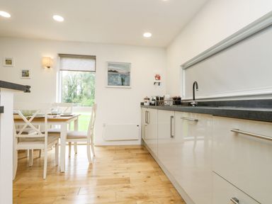 A kitchen with white cabinets a black countertop and a dining table with chairs at Birch in Truro