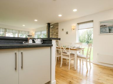 A dining area with a wooden table and white chairs next to large windows and a kitchen counter at Birch in Truro