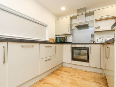 A kitchen with white cabinets black countertops a microwave toaster stove oven and wooden floor at Birch in Truro
