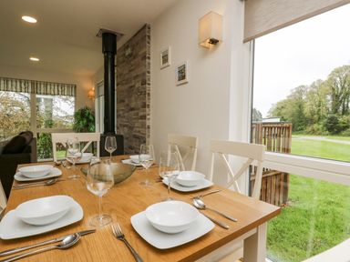 A dining table set for six with plates glasses and cutlery next to large windows showing green grass and trees at Birch in Truro