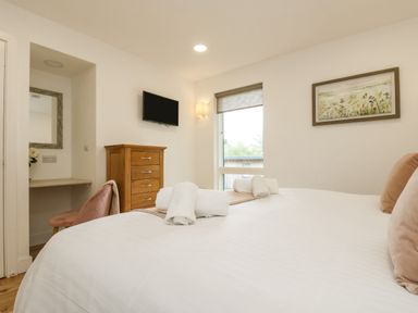 A bedroom with a bed with pillows and rolled towels a wooden chest of drawers a wall-mounted TV a window a chair and a desk at Birch in Truro