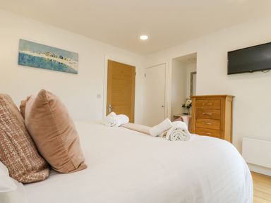 A bedroom with a bed with pillows and towels a wooden chest of drawers a wall-mounted tv and a door at Birch in Truro