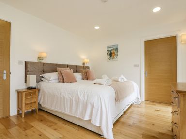 A bedroom with a large bed with white linens and beige pillows beside wooden doors and furniture at Birch in Truro