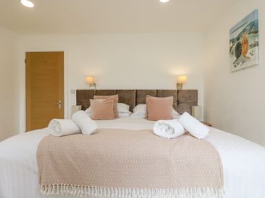 A bedroom with a bed with rolled towels pillows and a blanket two wall lights a door and a painting at Birch in Truro