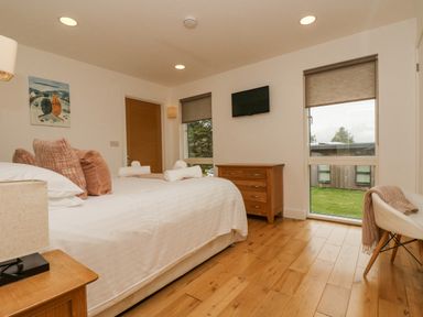 A bedroom with a bed pillows and towels a wooden dresser a wall-mounted tv and windows at Birch in Truro