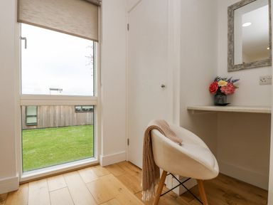 A small corner with a white chair and a desk with flowers and a mirror at Birch in Truro