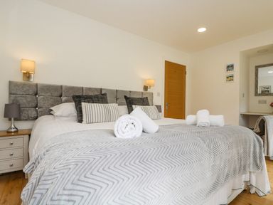 A bedroom with a large bed with a grey headboard and rolled white towels on the bed at Birch in Truro