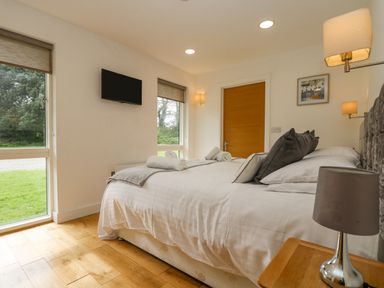 A bedroom with a bed with pillows and rolled towels a wall mounted tv wooden floor and windows at Birch in Truro
