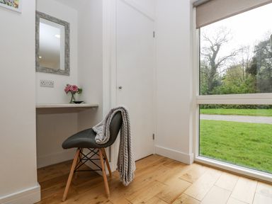 A small desk area with a chair and a blanket next to a large window showing green grass and trees at Birch in Truro
