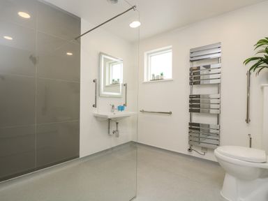 A bathroom with a wall-mounted sink a toilet a heated towel rail a small window and a walk-in shower at Birch in Truro