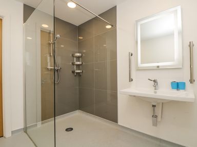 A bathroom with a walk in shower with glass partition a sink with a mirror above and two blue cups at Birch in Truro