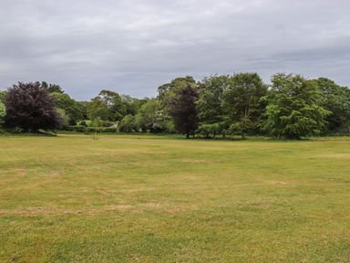An open grass field with scattered trees in the background under a cloudy sky at Elm in Truro
