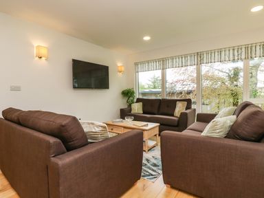 A living room with three brown sofas a wooden coffee table a wall-mounted television and large windows with patterned blinds at Elm in Truro
