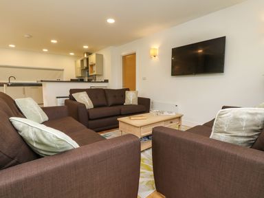 A living room with three brown sofas and cushions around a wooden coffee table with a TV mounted on the wall at Elm in Truro