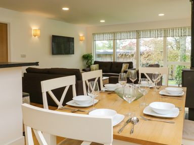 A dining table set with white dishes and glassware next to a living area with sofas and a wall-mounted TV at Elm in Truro