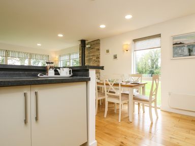 A kitchen counter and a dining table with chairs set near large windows overlooking the garden at Elm in Truro
