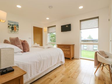 A bedroom with a bed with pillows and towels a wooden dresser a wall-mounted TV two windows with blinds and a chair with a blanket at Elm in Truro