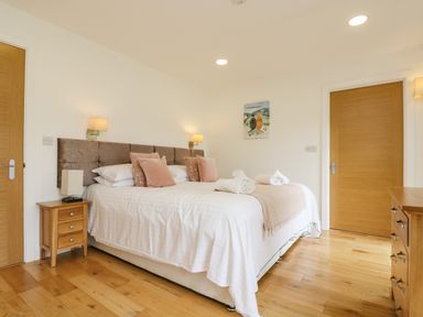A bedroom with a bed with white linens and pink pillows two wooden doors a wooden nightstand and a dresser at Elm in Truro