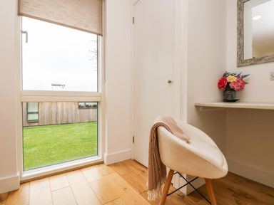 A room corner with a white chair holding a blanket a large window and a countertop with flowers at Elm in Truro