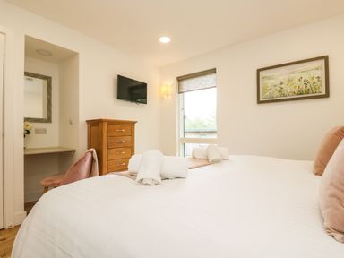 A bedroom with a bed, rolled white towels, a wooden dresser, a wall-mounted TV, a window with a blind, a chair, and a framed painting at Elm in Truro