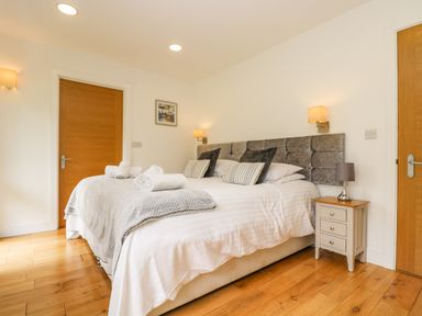 A bedroom with a double bed with pillows and rolled towels bedside tables with lamps wooden doors and wooden floor at Elm in Truro
