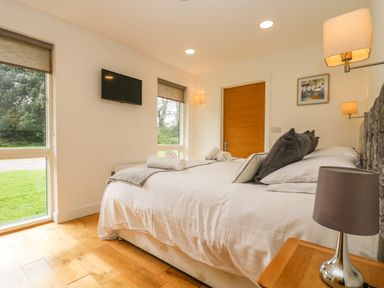 A bedroom with a double bed white bedding pillows folded towels wooden bedside table lamp wall mounted tv two windows door at Elm in Truro